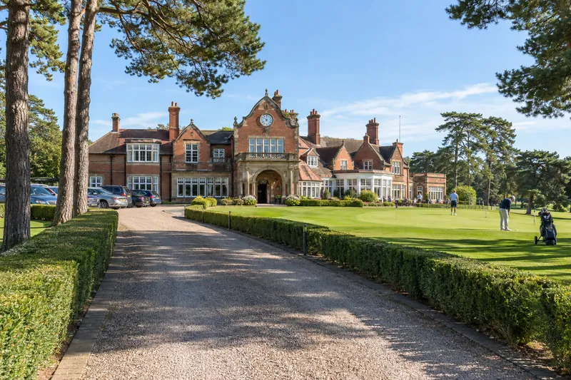 The gravel drive to the Edwardian clubhouse at Wrenmoor Heath, between clipped hedges and tall Scots pines.